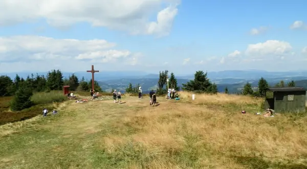 Wielka racza szlaki to widok na szczyt z krzyżem i ludźmi odpoczywającymi na trawie.