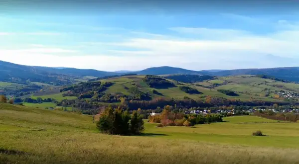 Malowniczy krajobraz z zielonymi wzgórzami i lasami, gdzieś w tle majaczy góra Grzywacka.