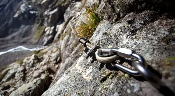 Stalowa lina i karabińczyk na skale, element ułatwiający wspinaczkę na via ferrata Czechy. Widok na zbocze.