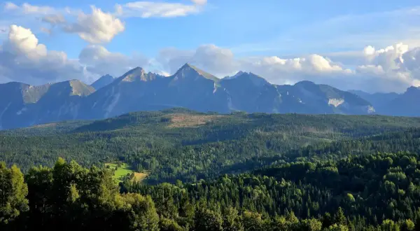 Widok na Tatry z przełęczy nad Łapszanką. Majestatyczne szczyty górskie na tle błękitnego nieba z chmurami.