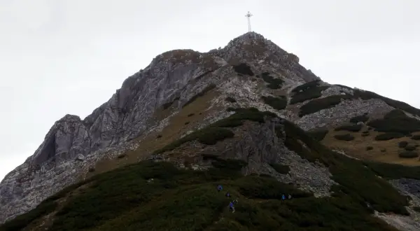 Grupa turystów wspina się po skalistej ścieżce na Giewont. Widoczny krzyż na szczycie. Trasa jest wymagająca.