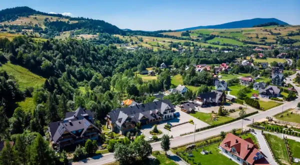 Malownicze gorce miejscowości z górami w tle, zielone wzgórza i urokliwe domy.
