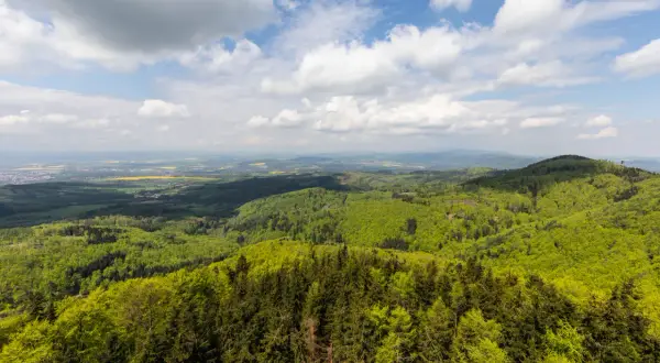 Widok z Kłodzkiej Góry na zielone wzgórza i pola. Niebo z chmurami.