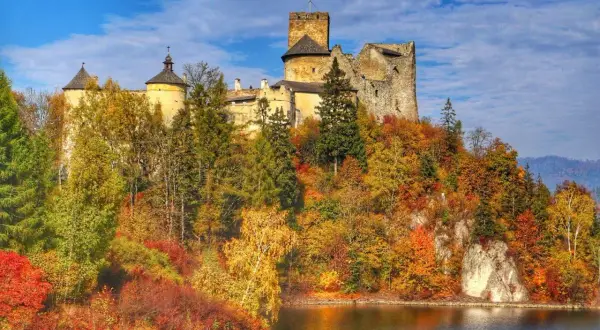 Zamek Dunajec w jesiennej szacie, otoczony kolorowymi drzewami, góruje nad spokojną taflą wody.