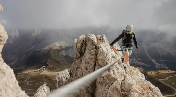 Kobieta na via ferrata, pokonująca skalną grań. Widok zapiera dech w piersiach, a droga jest wyzwaniem.