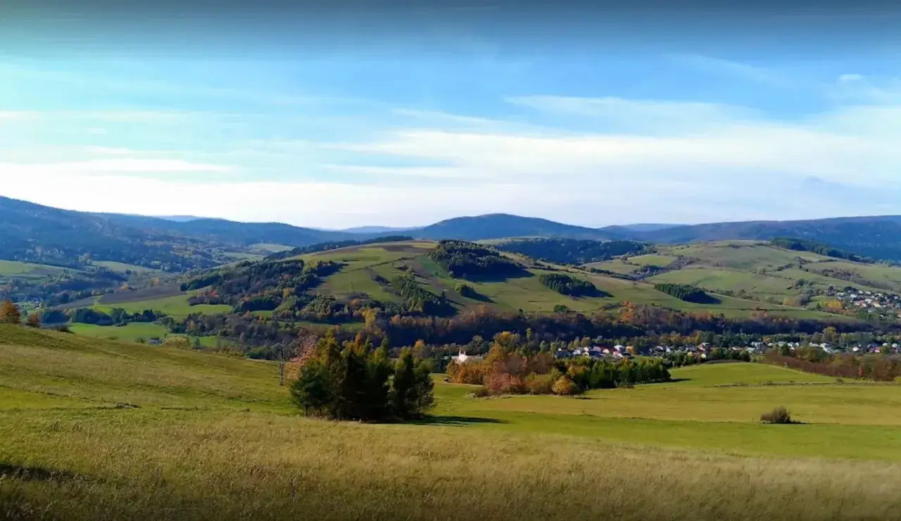Malowniczy krajobraz z zielonymi wzgórzami i lasami, gdzieś w tle majaczy góra Grzywacka.