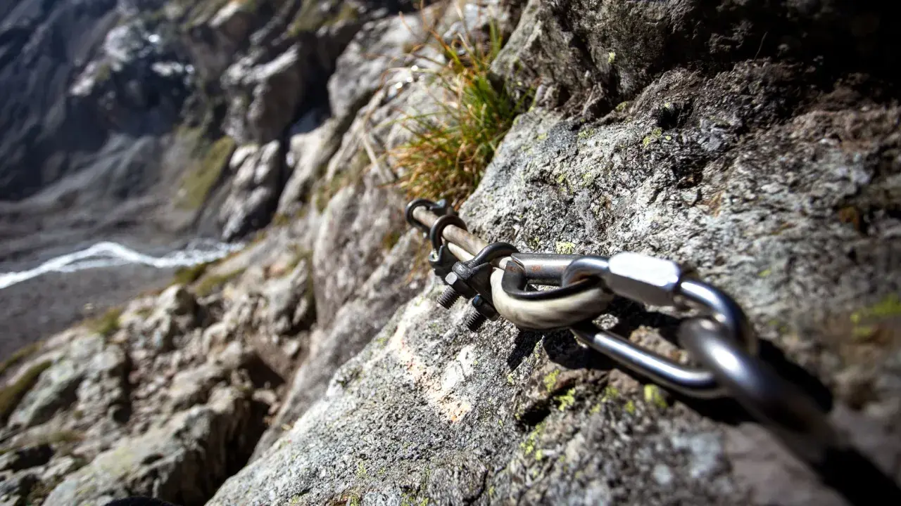 Stalowa lina i karabińczyk na skale, element ułatwiający wspinaczkę na via ferrata Czechy. Widok na zbocze.