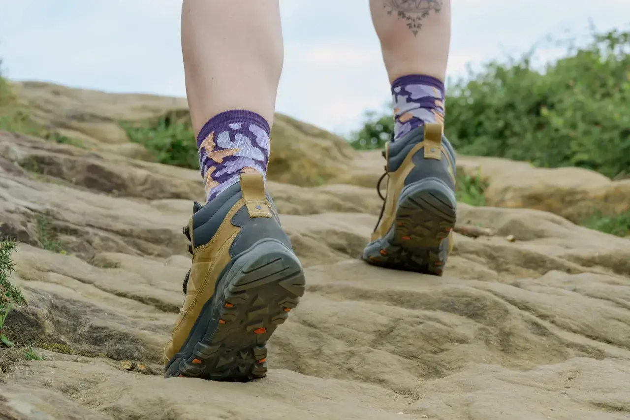 Wędrowiec stawia kroki po kamienistym szlaku, a jego **ciepłe stopy** w kolorowych skarpetkach i solidnych butach trekkingowych są gotowe na każdą przygodę.