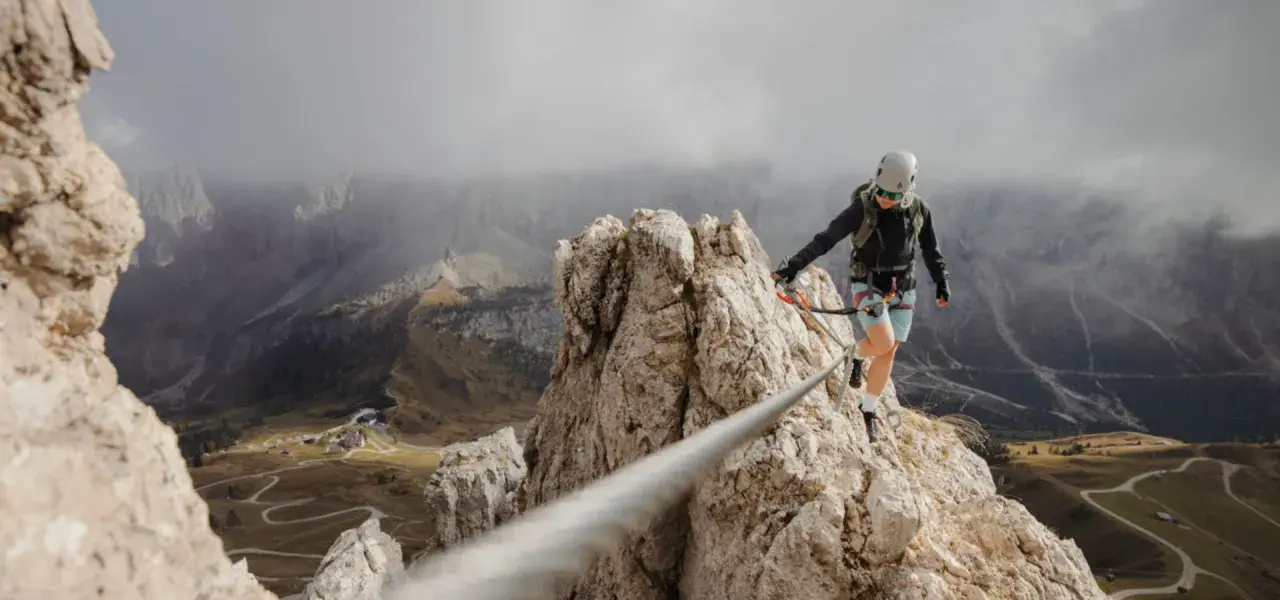 Kobieta na via ferrata, pokonująca skalną grań. Widok zapiera dech w piersiach, a droga jest wyzwaniem.