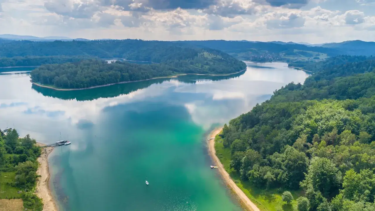Bieszczady atrakcje: malownicza zatoka jeziora Solińskiego z łodziami i otaczającymi ją zielonymi wzgórzami.