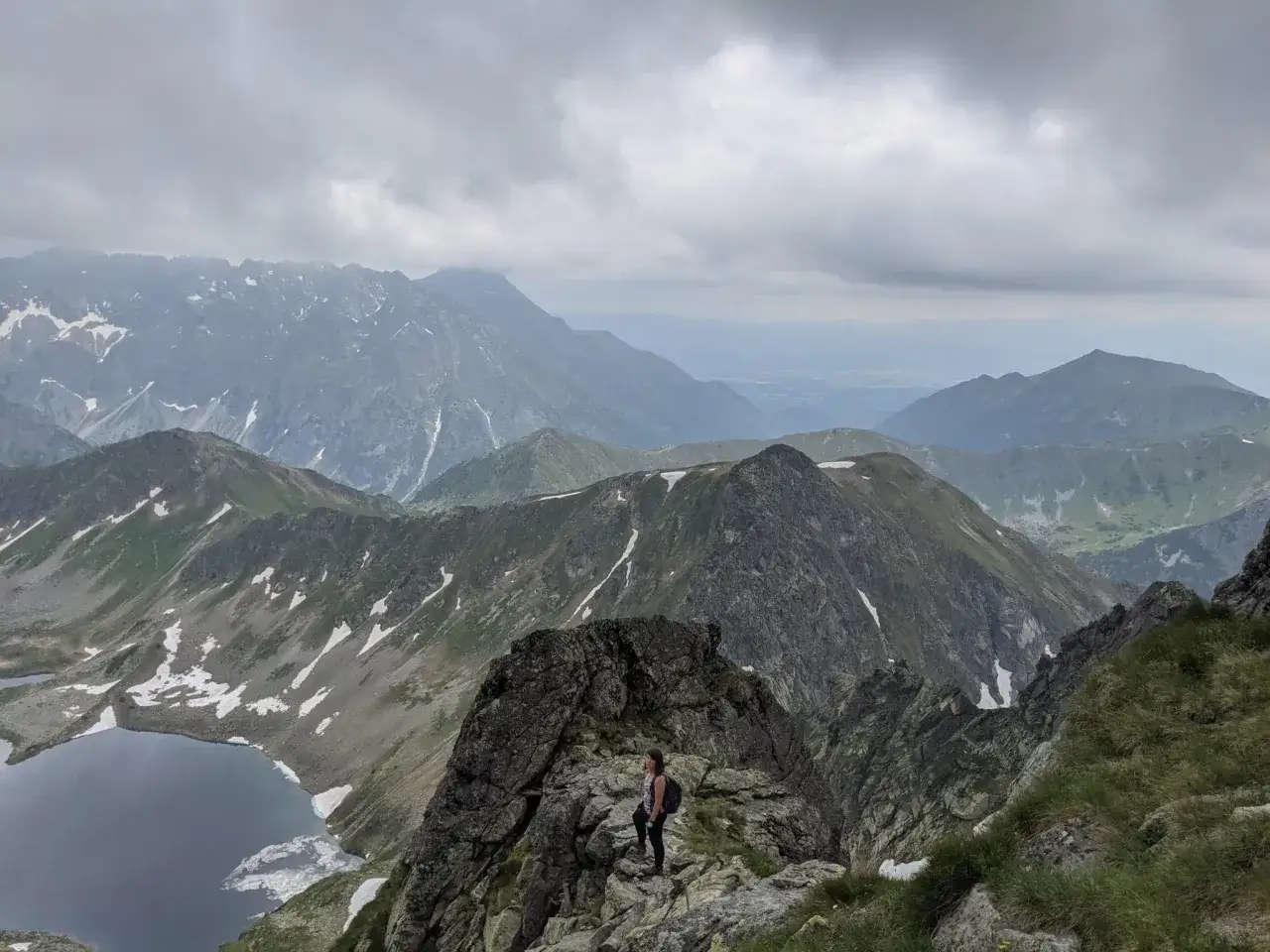 Widok z zawrat szczyt na Tatry. Kobieta z plecakiem na skalistym szczycie, w dole jezioro.