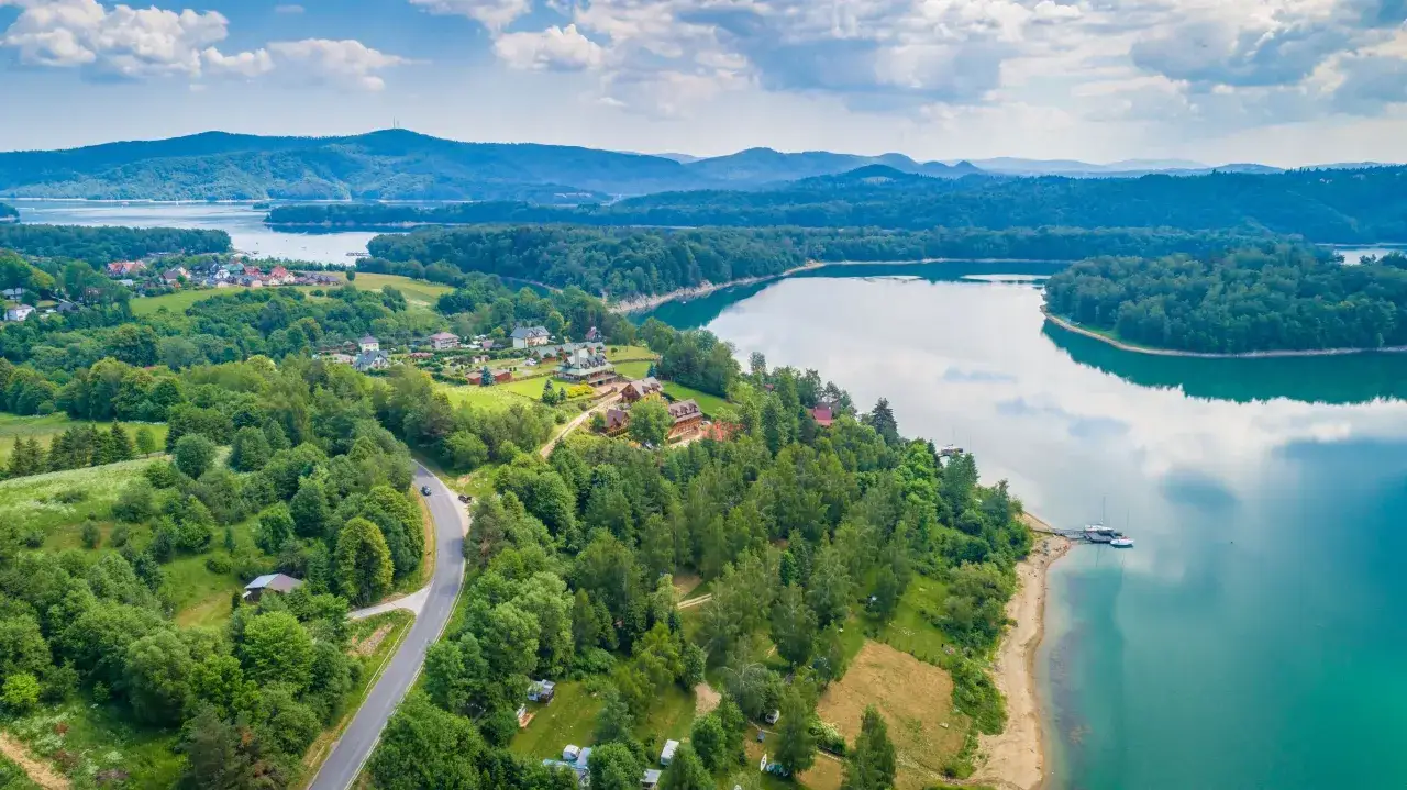 Malownicze Bieszczady oferują piękne widoki i liczne atrakcje. Jezioro Solińskie otoczone zielonymi wzgórzami, z urokliwymi domkami i żaglówkami.