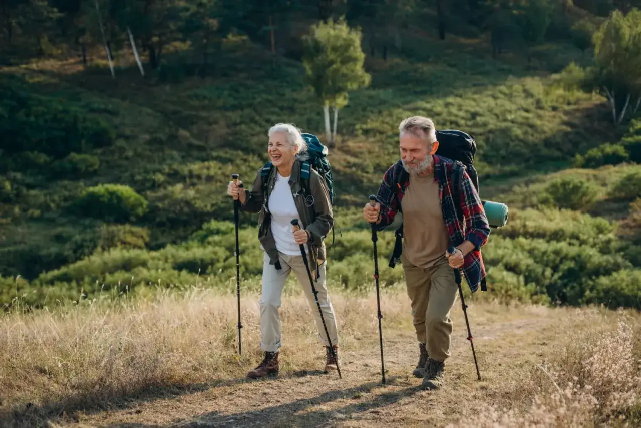 Uśmiechnięta para senior&oacute;w wyruszyła na wędr&oacute;wkę. Ich aktywność fizyczna, czyli nordic walking, pozwala cieszyć się pięknem natury i zdrowiem.
