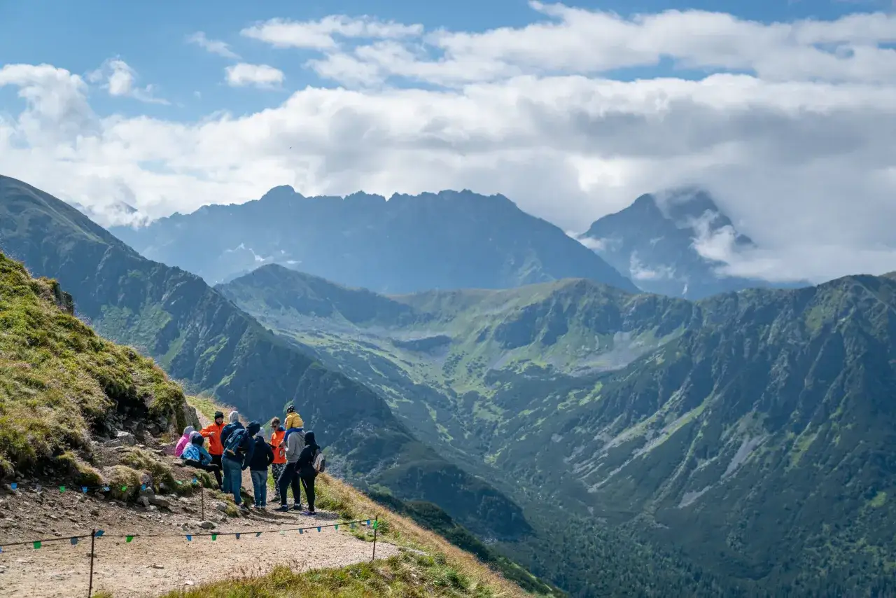 Grupa turystów na szlaku, podziwiająca majestatyczne Tatry. Widok zapiera dech w piersiach, a Kasprowy Wierch wysokość robi wrażenie.