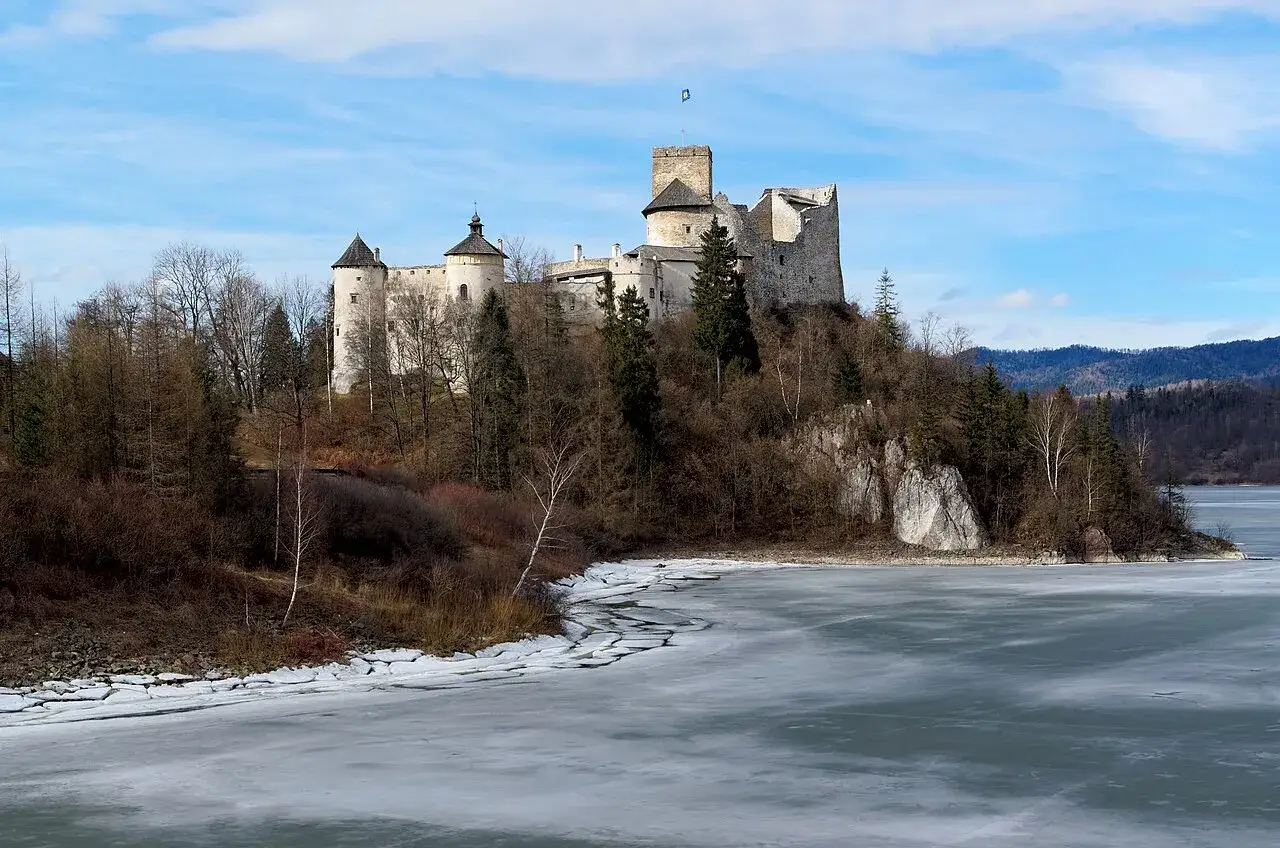 Zamek Dunajec majestatycznie wznosi się na wzg&oacute;rzu nad zamarzniętym jeziorem, otoczony zimową przyrodą.