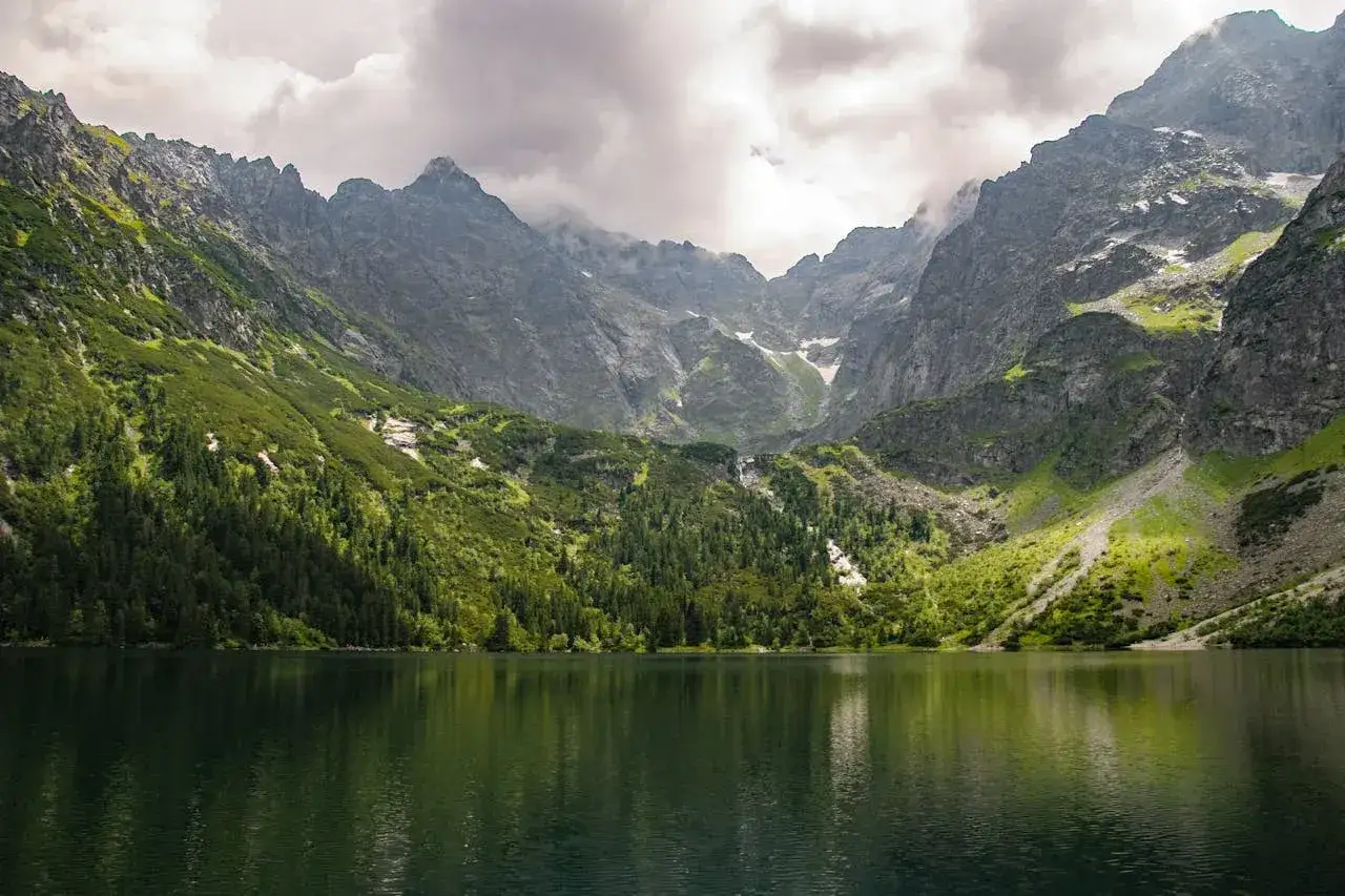 Jezioro Morskie Oko otoczone stromymi, zielonymi zboczami Tatr. Idealne miejsce, gdzie najlepiej jechać w góry, by podziwiać majestatyczne krajobrazy.