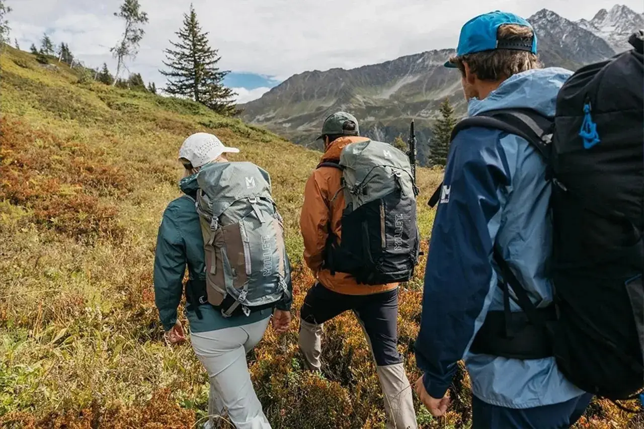 Trzy osoby w plecakach idące po g&oacute;rskim szlaku. To właśnie jest trekking &ndash; przygoda na łonie natury.