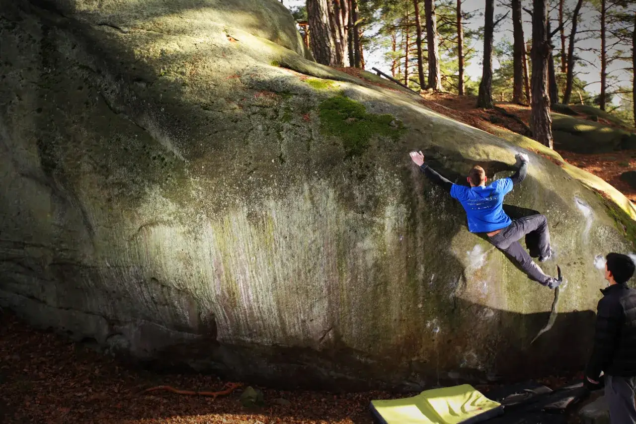 Mężczyzna wspina się po skale, pokazując, bouldering co to jest. W lesie, na tle drzew, wspinaczka bez liny.