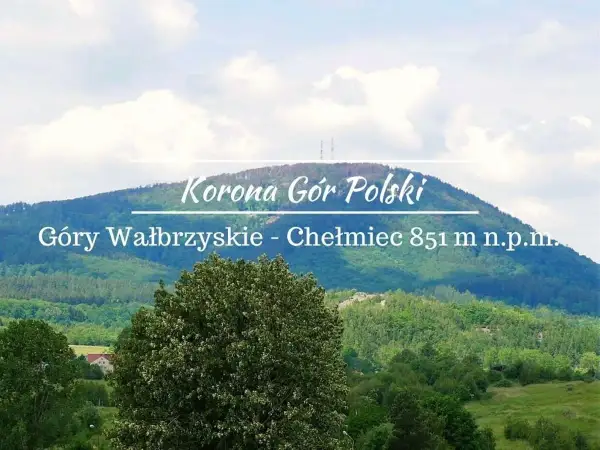 Widok na górzysty krajobraz z dominującym szczytem Chełmiec. Na pierwszym planie bujna zieleń drzew, w tle łagodne zbocza Gór Wałbrzyskich.