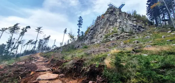 Kamienista ścieżka prowadzi ku skalnej grani z platformą widokową. To szlak na Trojak w Lądku-Zdroju, otoczony dziką przyrodą.