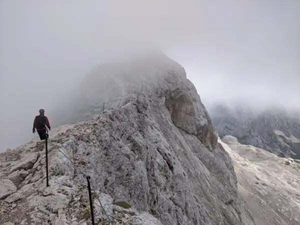 Turysta na skalistej ścieżce, wspinający się po via ferracie. Mgła otula szczyty, tworząc mistyczną atmosferę na szlakach Triglavu.