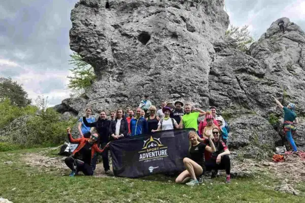 Grupa entuzjastów wspinaczki na Jurze Krakowsko-Częstochowskiej pozuje do zdjęcia z banerem "Sport Adventure".