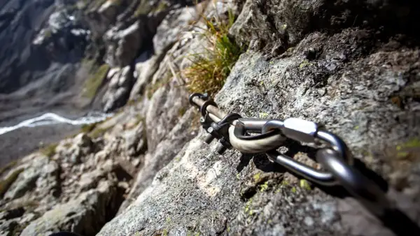 Stalowa lina i karabińczyk na skale, element ułatwiający wspinaczkę na via ferrata Czechy. Widok na zbocze.