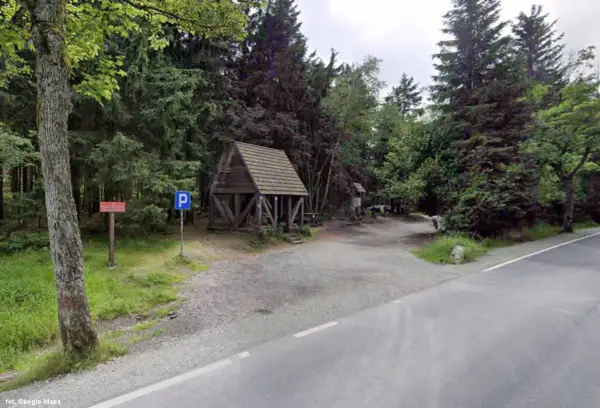 Drewniana wiata i parking przy leśnej drodze. To miejsce to Lisia Przełęcz, idealne na odpoczynek w otoczeniu drzew.