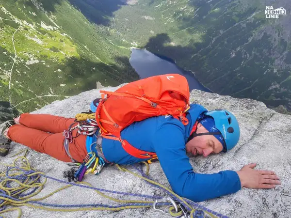Zmęczony wspinacz odpoczywa na skale po wejściu na mnicha. Widok na jezioro i góry.