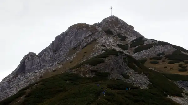 Grupa turystów wspina się po skalistej ścieżce na Giewont. Widoczny krzyż na szczycie. Trasa jest wymagająca.